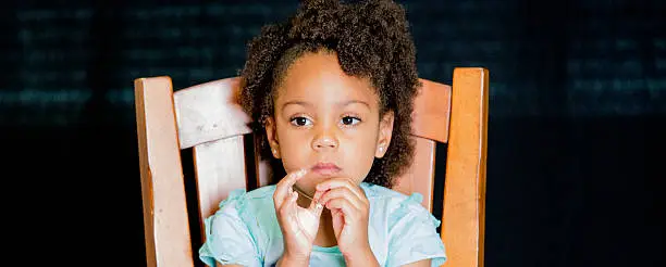 African American young girl/child with natural hair pose sitting no smile while playing with her necklace.