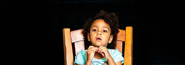 African American young girl/child with natural hair pose sitting with mouth open as if she is saying huh while playing with her necklace