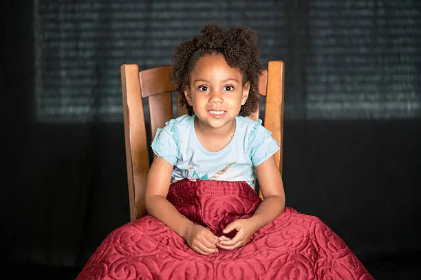 African American young girl/child with natural hair pose sitting under a cover looking forward fiddling with her hands.