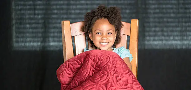 African American young girl/child with natural hair pose sitting under a cover where she is pulling it up with a big smile