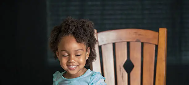 African American young girl/child with natural hair pose standing next to a chair with eyes closed