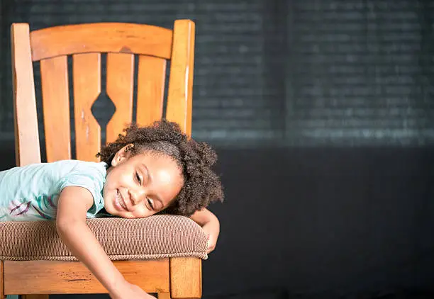 African American young girl/child with natural hair pose laying across a chair with eyes half closed.