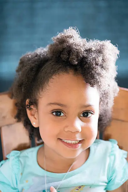 African American young girl/child with natural hair pose sitting playing with necklace and smiling.