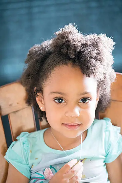 African American young girl/child with natural hair pose sitting playing with necklace and no smile looking forward.
