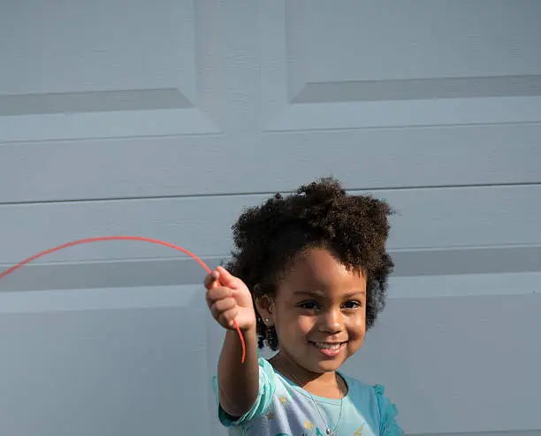 African American young girl/child with natural hair turning into sunlight playing with a string rope typed item.