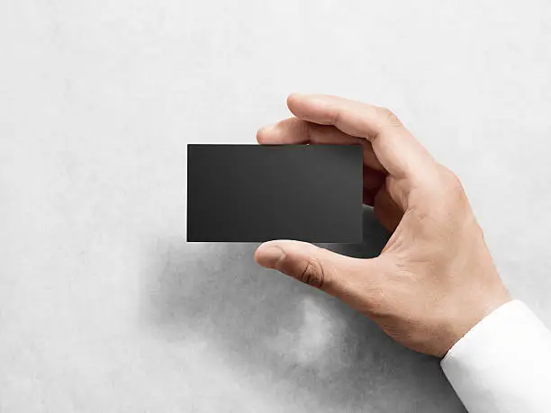 Photo of Hand holding blank plain black business card design mockup.