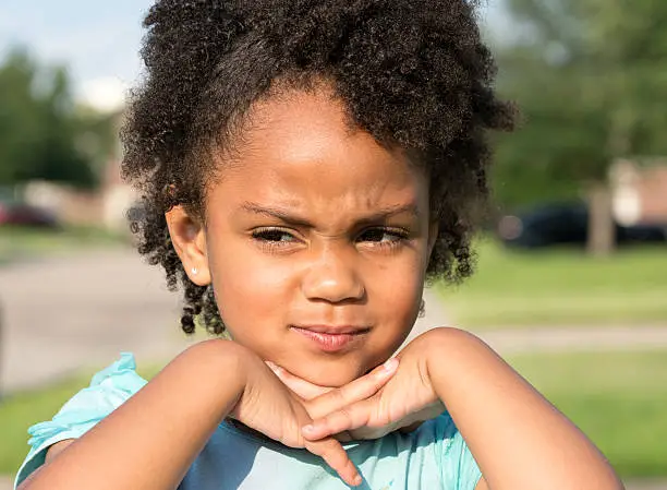African American young girl/child with natural hair standing looking away with fingers crossed interlocked under chin.