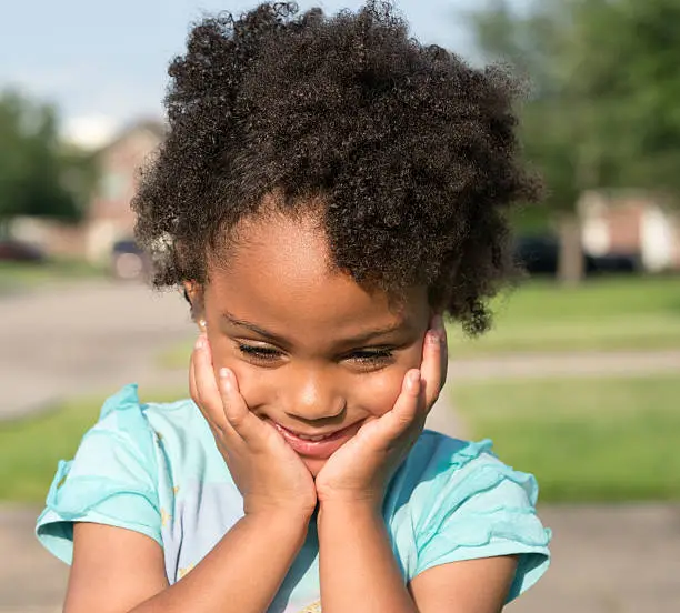 African American young girl/child with natural hair standing looking down with fingers hands under chin.