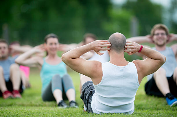 Doing Sit Ups at the Park A multi-ethnic group of young adults are working out together during a bootcamp class at the park. They are doing sit ups in the grass. fitness boot camp stock pictures, royalty-free photos & images