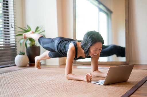 Asian woman exercising at home following a fitness video online