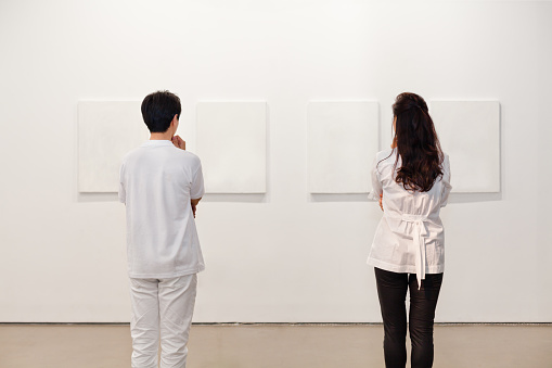 Man and woman looking at white frames in an art gallery