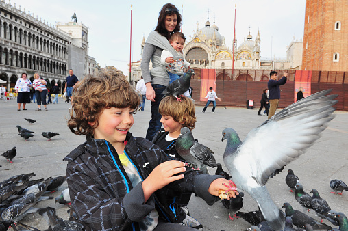 Venice, Italy - April 30, 2011: Visitors play with pigeons in St Mark's Square, Venice Italy. Each year the town receives 18 million tourists. This equates to approximately 50,000 visitors each day.