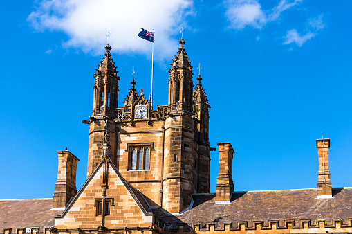 Sydney Uni building facade with Australian flag. University of Sydney against deep blue sky with white clouds, daytime photo