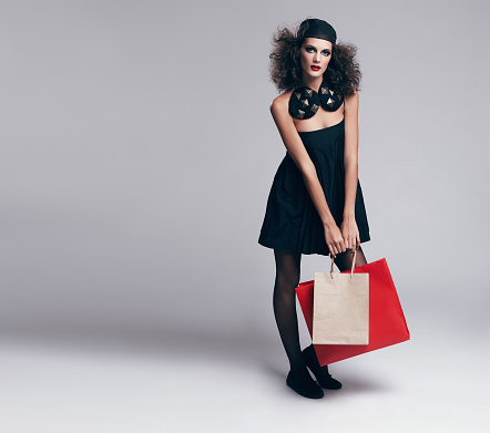 Studio portrait of a beautiful young fashion model carrying shopping bags against a gray background