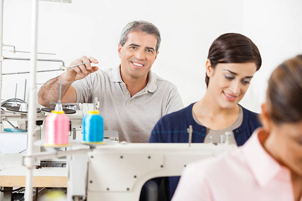 istock Happy Tailor Sitting With Colleagues Working In Sewing Factory 542943642