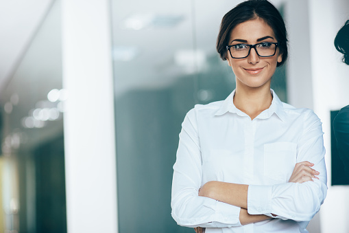 Portrait of young woman wearing white shirt and glasses, with arms crossed and copy space