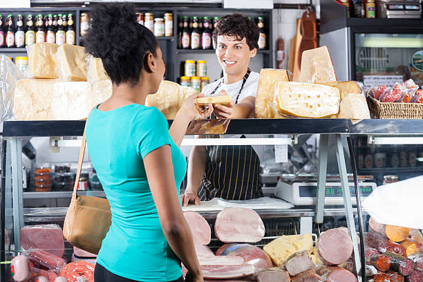 lächelnder verkäufer, der käse an weibliche kunden verkauft - feinkostgeschäft stock-fotos und bilder