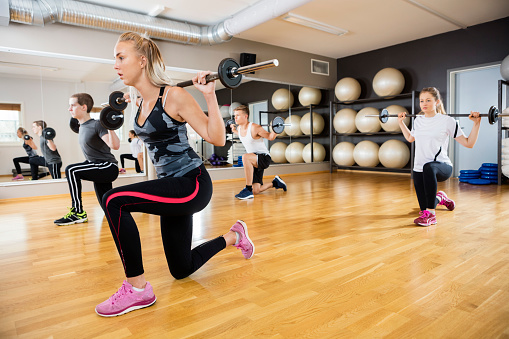 Young female and male friends lifting barbells in gym