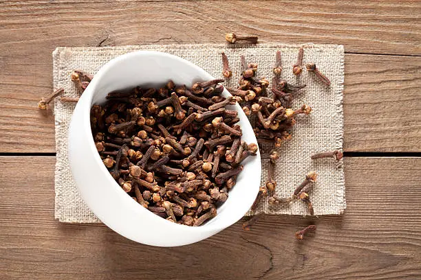Close up of cloves in cup on old wooden table. This file is cleaned and retouched.