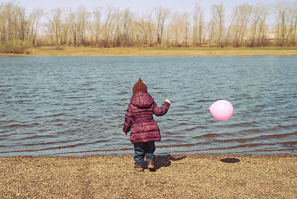 Little girl with a pink balloon on riverbank Little girl with a pink balloon standing on a riverbank in spring time backside for a girl on the beach stock pictures, royalty-free photos & images