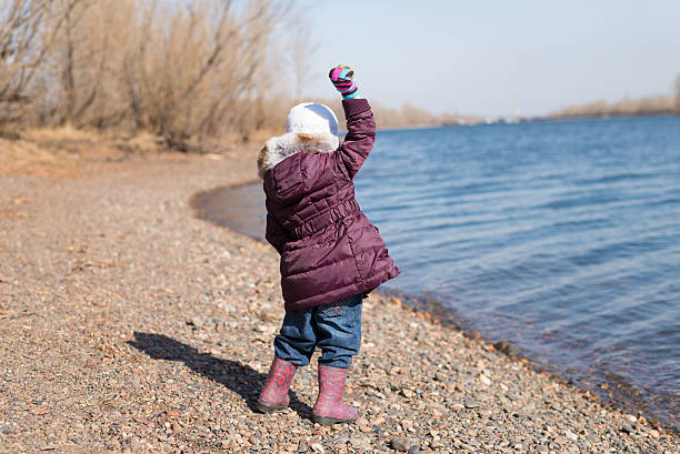 Girl throwing stones into river Little girl throwing stones into river in spring backside for a girl on the beach stock pictures, royalty-free photos & images