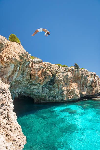 Guy jumping off a Cliff into the Ocean, Mallorca, Spain Guy jumping a backflip off a Cliff into the Ocean, Mallorca, Spain. Nikon D810. Converted from RAW. cliff jumping stock pictures, royalty-free photos & images