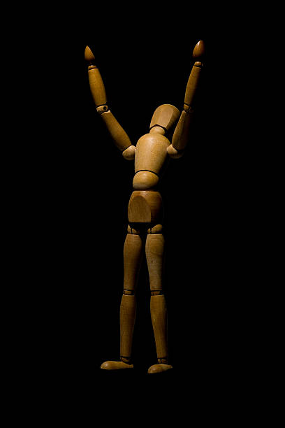istock Wooden mannequin raising hands to light isolated on black. 542954078