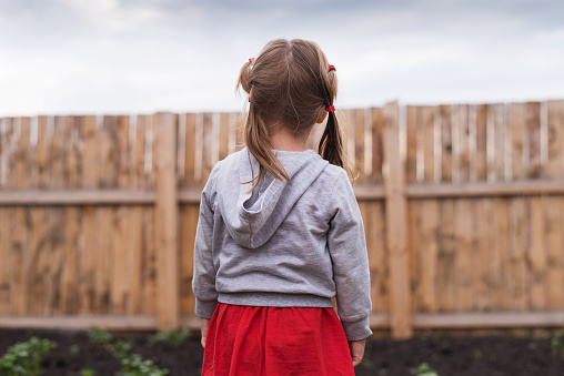 Little girl standing in front of a wooden fence in the garden on a summerday.