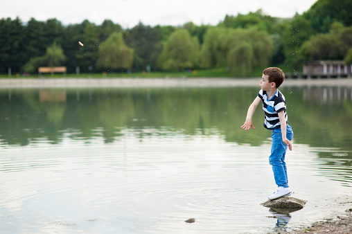 active boy throws small stone into the lake