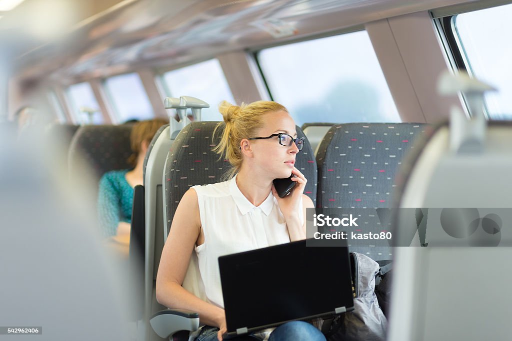 Business woman working while travelling by train. Businesswoman talking on cellphone and working on laptop while traveling by train. Business travel concept. Commuter Stock Photo