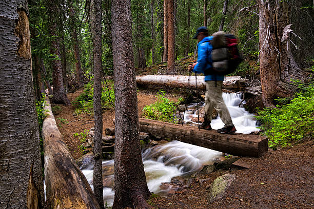 Hiker Crosses Bridge Over Mountain Creek - Deep in a forest with pristine creeks flowing. Hiker recreating and crosses bridge while backpacking in wilderness.