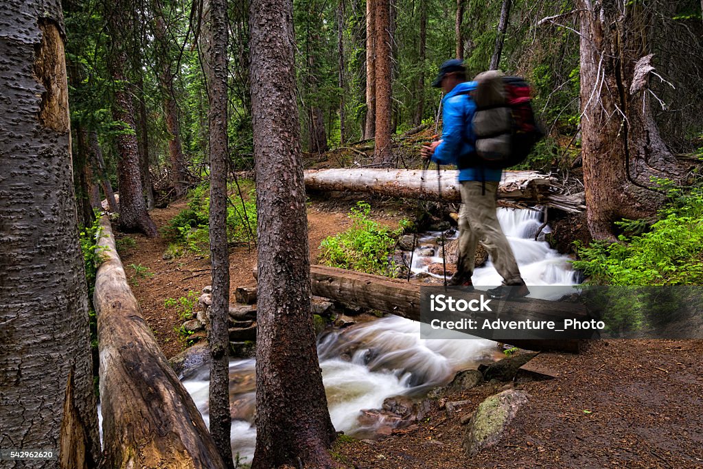 Hiker Crosses Bridge Over Mountain Creek Hiker Crosses Bridge Over Mountain Creek - Deep in a forest with pristine creeks flowing. Hiker recreating and crosses bridge while backpacking in wilderness. Vail - Colorado Stock Photo