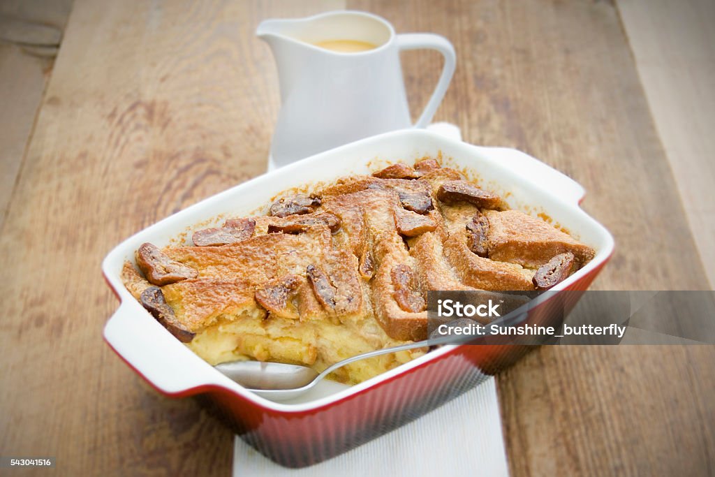 Bread and Butter Pudding with Custard Traditional British Dessert, Bread and Butter Pudding with Custard. Served in a red oven dish on wood.  Bread Dessert Stock Photo