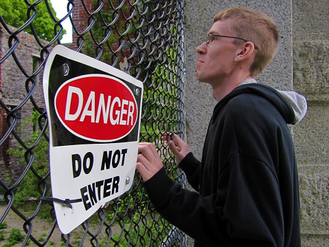 Young man blocked by fence with Do Not Enter sign.