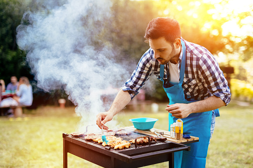 Handsome male preparing barbecue outdoors for friends