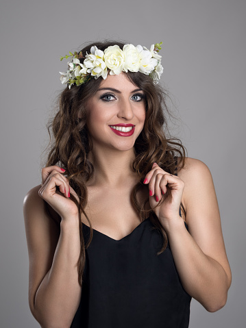 Beautiful girl with flowers in hair posing in black shirt looking at camera over gray studio background