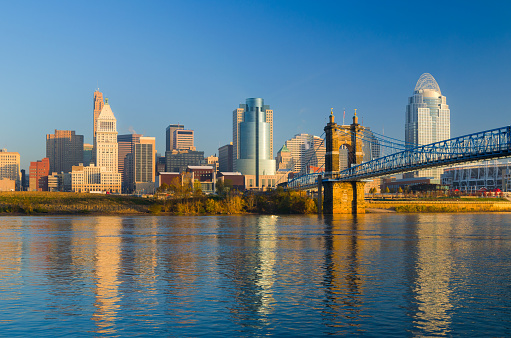 Downtown Cincinnati skyline during the early morning, with the Ohio River and the Roebling Suspension Bridge in the foreground.
