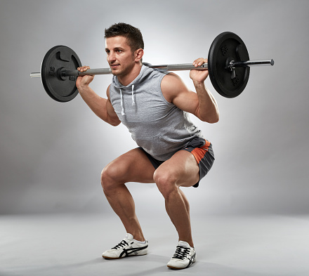 Man doing squats with barbell on neck back, studio shot