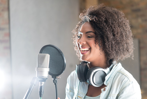 Beautiful young woman smiling behind the microphone at a recording studio and looking very happy
