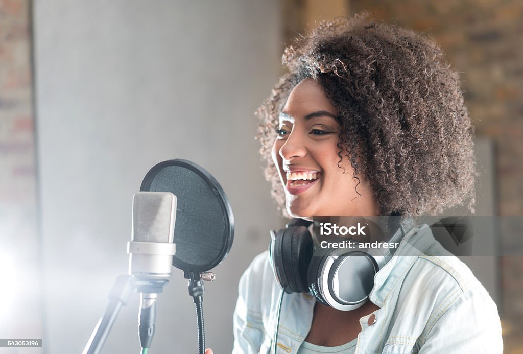 Happy woman at a recording studio Beautiful young woman smiling behind the microphone at a recording studio and looking very happy Singer Stock Photo