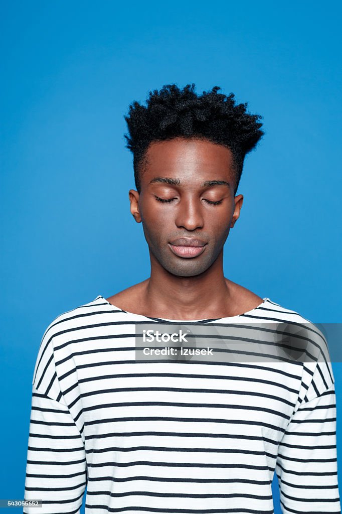 Afro american guy closing eyes Portrait of serious afro american young man wearing striped top, closing eyes. Studio portrait, blue background. Adult Stock Photo