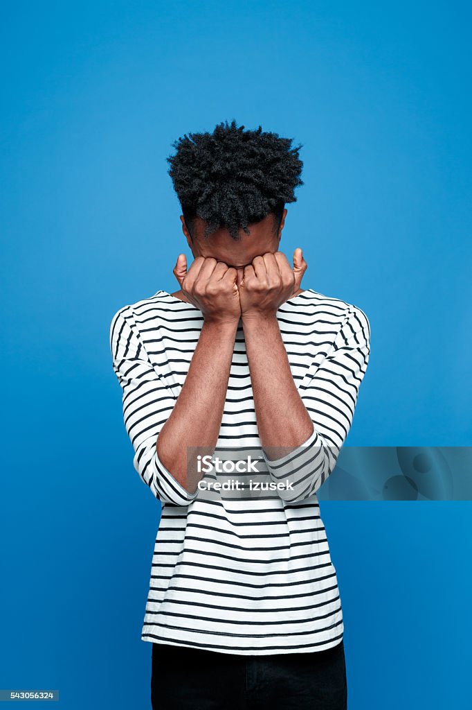 Afro american guy crying Portrait of worried afro american young man wearing striped top, crying. Studio portrait, blue background. Colored Background Stock Photo