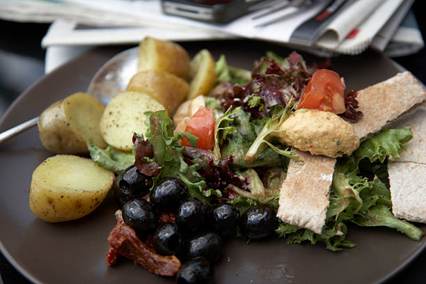 A plate of fresh summer salad comprising of ,olives, jersey Royal potatoes,sun dried tomatoes,leavy salad with dressing. photographed cloe proximity: daily newspaper and mobile phone slightly out of focus in foreground.A plate of fresh summer salad comprising of ,olives, jersey Royal potatoes,sun dried tomatoes,leafy salad with dressing. photographed close proximity: daily newspaper and mobile phone slightly out of focus in foreground.