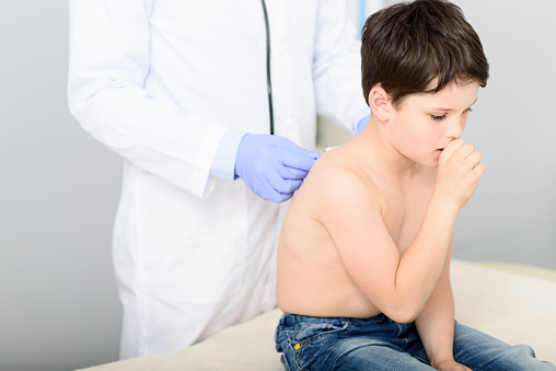 I worry about your cough. Little boy coughing at doctor checkup, sitting at his office