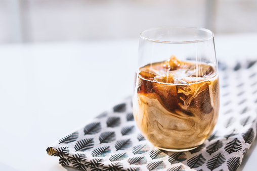 Coffee ice cubes with milk in glass cup on leaf patterned tea towel.