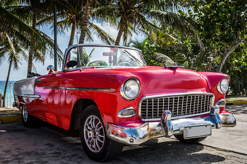 American red classic car parked under palms near the beach in Havana Cuba
