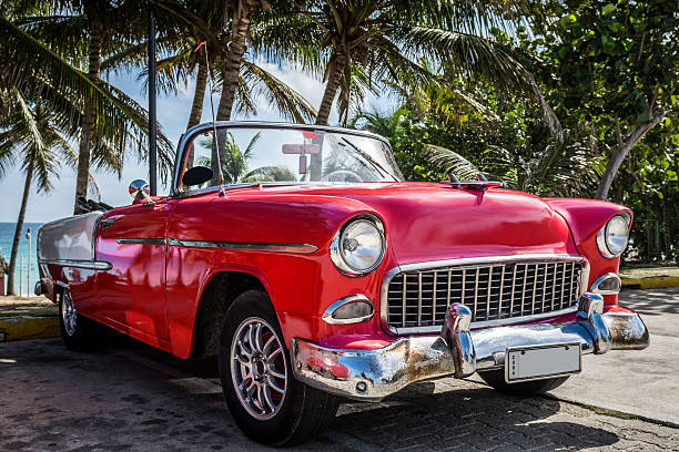 American red classic car parked under palms near the beach stock photo