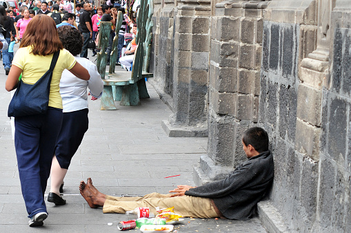 Mexico City, Mexico - February 23, 2010: Women walk past a Mexican man homeless in Mexico City Mexico. 44 percent of the Mexican population, over 49 million, lives below the poverty line.