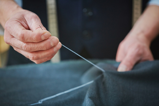 Hands of experienced tailor sewing at work