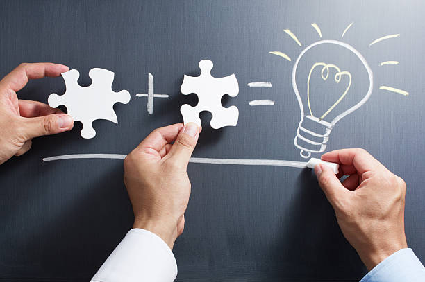 Solving puzzle together. Drawing light bulb on blackboard. stock photo